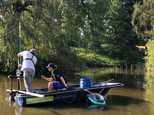 Die zwei Männer auf dem Boot entnehmen Schlammproben vom Boden des Teiches